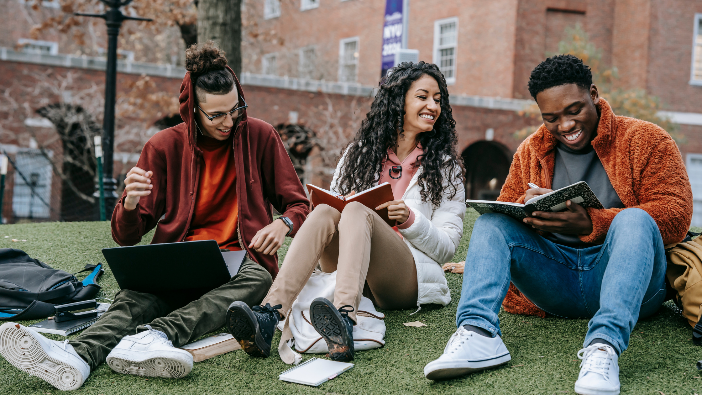 A group of students sitting on a grass patch with their laptops and books